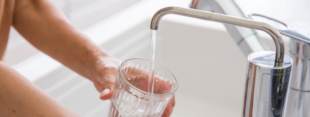 Die Hand einer Frau füllt ein Glas Wasser aus einem Wasserfilter.